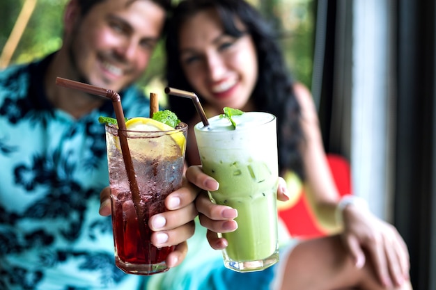 Молодая счастливая пара пьет вкусные сладкие коктейли в тропическом баре, улыбается и веселится, яркая одежда и положительные эмоции.