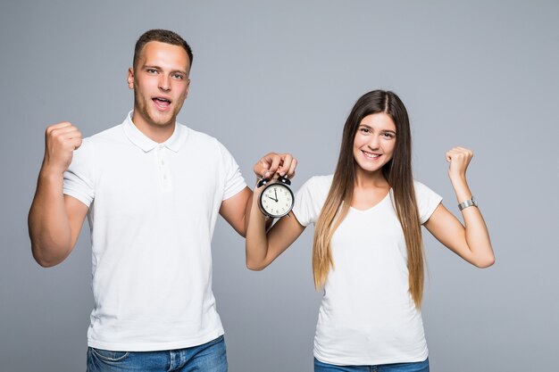 Young happy couple full of energy holding alarm clock dressed up in white tshirts