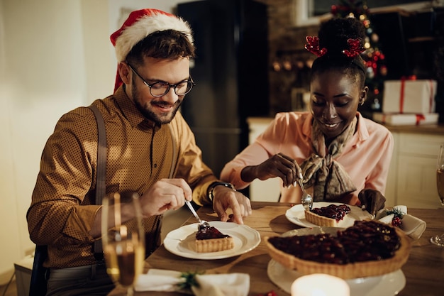 Young happy couple having cranberry pie during Christmas dinner at home