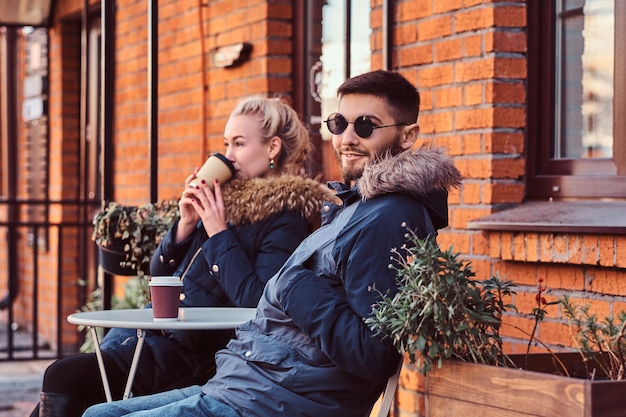 若い幸せなカップルは、屋外のカフェでコーヒーを飲みながら、一緒に時間を過ごしています。