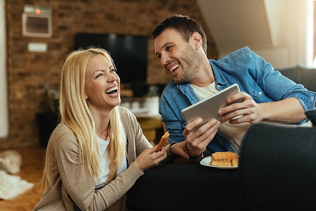 Young happy couple laughing while watching something funny on touchpad at home.