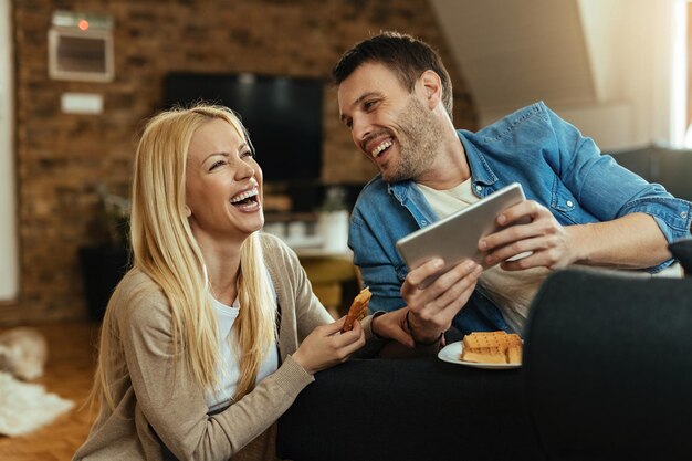 Young happy couple laughing while watching something funny on touchpad at home.