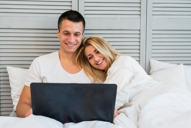 Young happy couple looking at laptop with blanket on bed