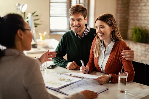 Young happy couple signing a contract while being on a meeting with insurance agent in the office