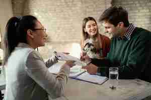 Free photo young happy couple signing document while having meeting with real estate agent in the office focus is on man