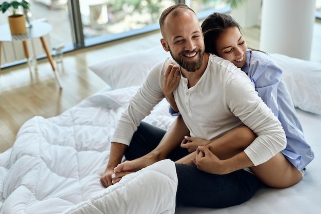 Young happy couple sitting embraced on a bed and having fun in the morning