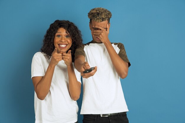 Young happy couple in white casual clothes posing on blue wall