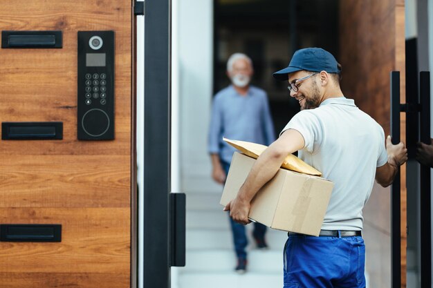 Young happy courier making home delivery His customer is standing in the background