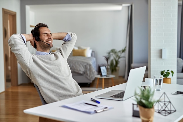Молодой счастливый предприниматель расслабляется с руками за головой после работы на компьютере дома
