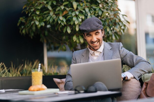 Young happy entrepreneur working on laptop while relaxing in outdoor cafe