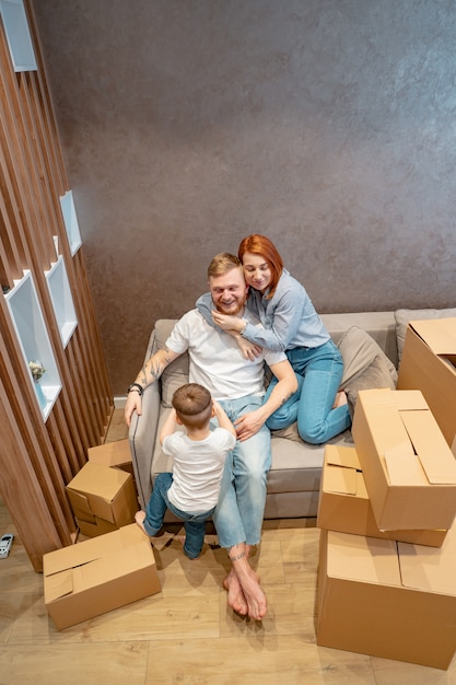 Бесплатное фото Молодая счастливая семья с ребенком, распаковка коробок вместе сидя на диване