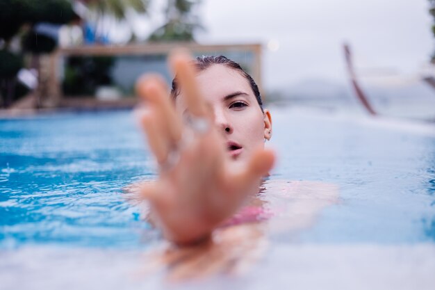 Young happy fit slim european woman in bright pink bikini blue swimming pool