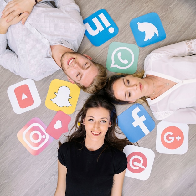 Free photo young happy friend lying on floor with social media logos