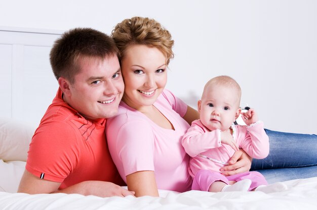 Молодая счастливая веселая семья с ребенком, лежащим на кровати у себя дома