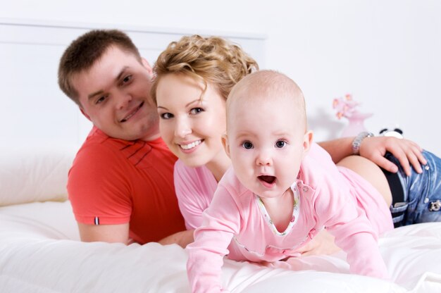 Young happy fun family with baby lying on bed at home