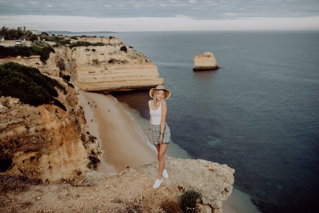 Молодая счастливая девушка на краю камня с панорамным видом на морской пляж.