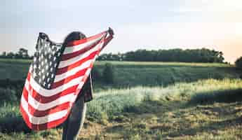 Free photo young happy girl running and jumping carefree with open arms over wheat field. holding usa flag.