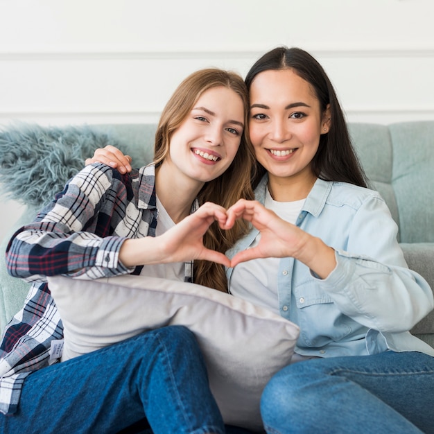 Young happy girlfriends showing heart sign