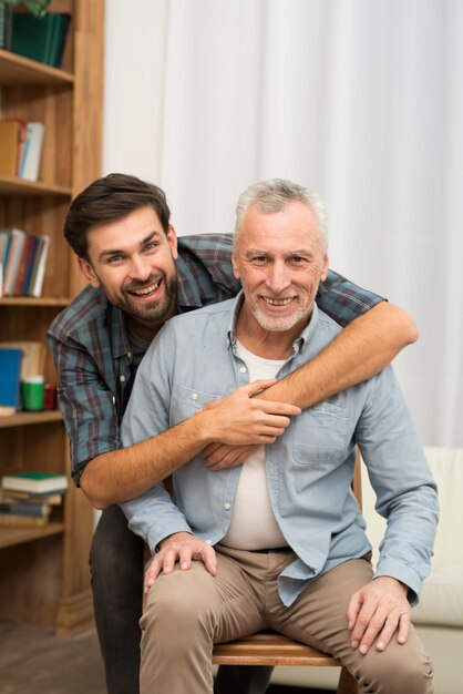 Young happy guy hugging aged man on chair