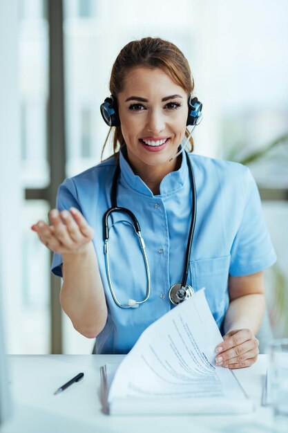 Young happy healthcare worker with headset working at medical hotline center and looking at camera