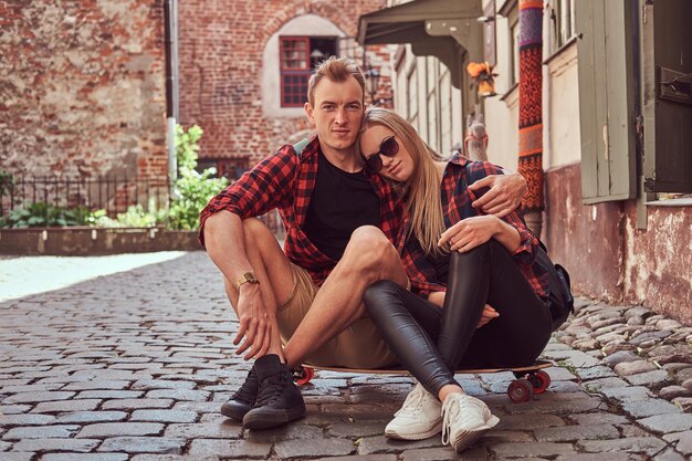 Young happy hipster couple, rest during a walk sitting on the pavement in the old Europe street.