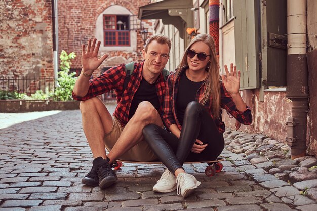 若い幸せな流行に敏感なカップルは、古いヨーロッパの通りの舗装に座って散歩中に休憩します。
