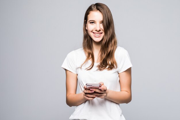 Молодая счастливая дама в белой футболке и синих джинсах остается с телефоном на белом фоне студии