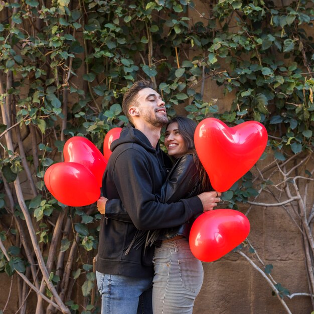 Young happy man hugging smiling woman and holding balloons in form of hearts