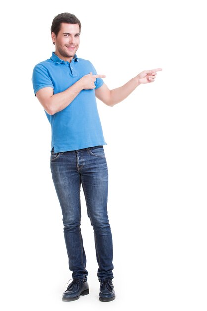 Young happy man shows a finger in the side in full length- isolated on white.