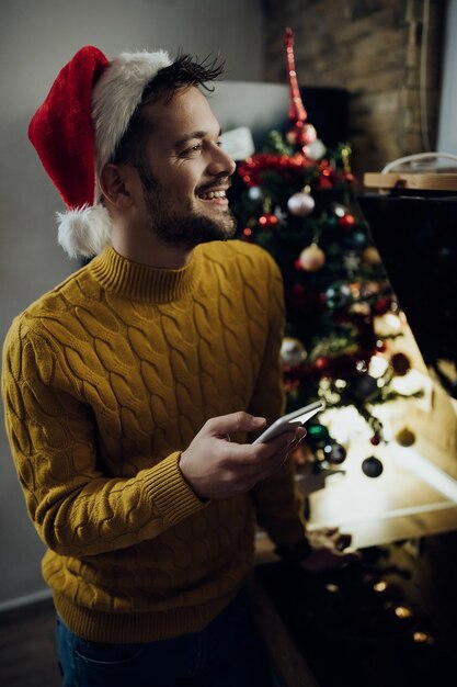 Молодой счастливый человек пишет смс на смартфоне в канун Нового года дома