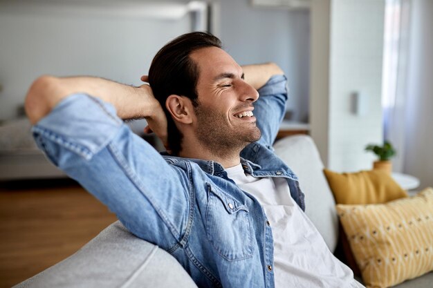 Молодой счастливый мужчина с руками за головой отдыхает дома на диване