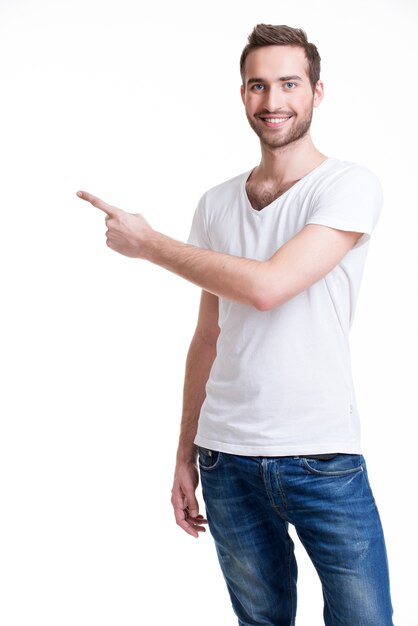 Молодой счастливый человек с показывает палец в сторону в повседневной одежде - изолированный на белом.
