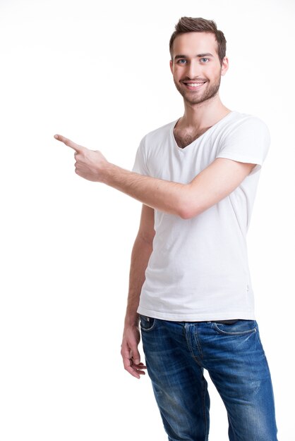 Young happy man with shows a finger in the side  in casuals  - isolated on white.