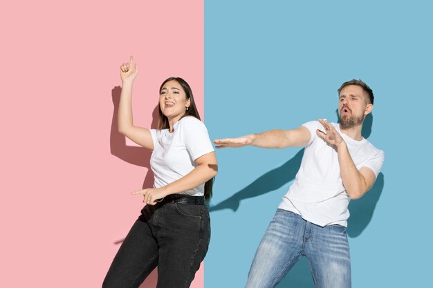 Young and happy man and woman in casual clothes on pink, blue bicolored wall, dancing