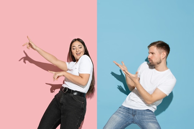 Young and happy man and woman in casual clothes on pink, blue bicolored wall, dancing