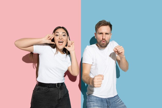 Young and happy man and woman in casual clothes on pink, blue bicolored wall, dancing