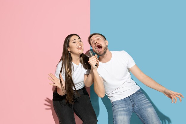 젊고 행복한 남자와 여자, 핑크, 블루 바이 컬러 벽에 캐주얼 옷, 노래