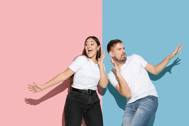 Young and happy man and woman in casual clothes on pink and blue bicolored wall