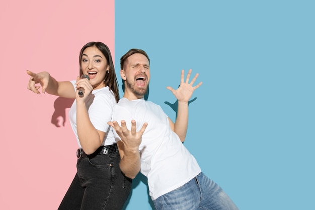 Young and happy man and woman in casual clothes on pink and blue bicolored wall