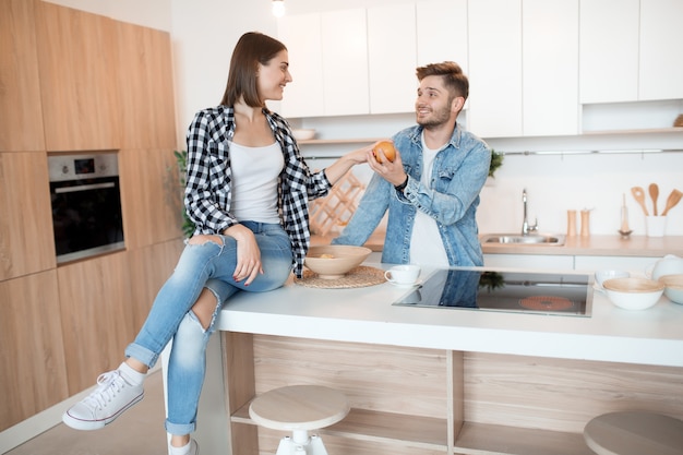 Giovane uomo felice e donna in cucina, colazione, coppia divertirsi insieme al mattino, sorridente, tenendo la mela