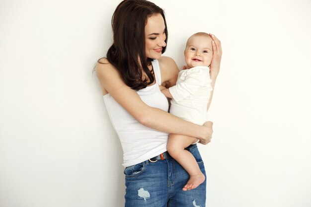Young happy mother smiling holding looking at her baby daughter over white wall.