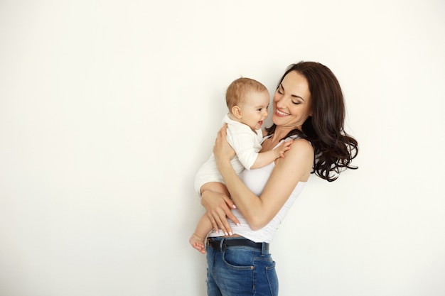 Young happy mother smiling holding looking at her baby daughter over white wall.