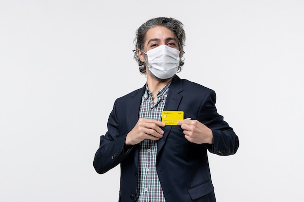 Young happy office assistant in suit wearing mask and holding his bank card on isolated white background