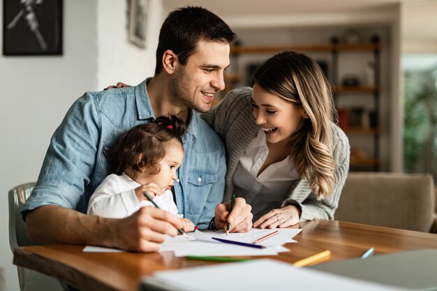 Young happy parents enjoying in coloring with their small daughter at home