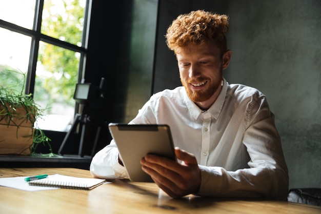 画面を見て、タブレットを使用して若い幸せなリードヘッドのひげを生やした男