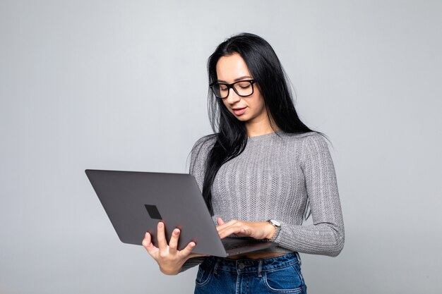 Young happy smiling woman in casual clothes holding laptop isolated on gray wall
