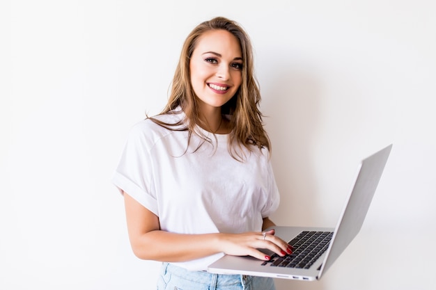 Young happy smiling woman in casual clothes holding laptop and sending email to her best friend