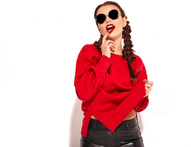 молодая счастливая улыбающаяся модель женщины с яркой косметикой и красочными губами с двумя косичками и солнцезащитными очками в летней красной изолированной одежде. касаясь ее рта