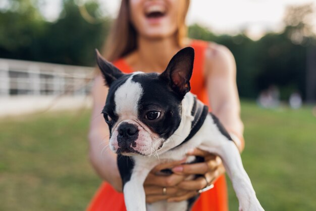 公園、夏のスタイル、陽気な気分で犬と遊ぶのを楽しんでオレンジ色のドレスで若い幸せな笑顔の女性