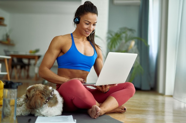 Free photo young happy sportswoman using computer while relaxing on the floor in the living room